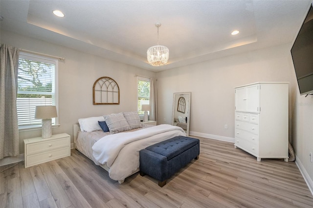 bedroom with light wood finished floors, a tray ceiling, a notable chandelier, and baseboards