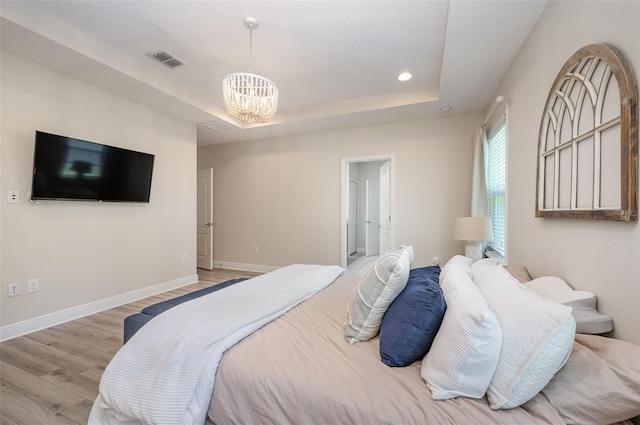 bedroom featuring a raised ceiling, visible vents, light wood-style flooring, a chandelier, and baseboards