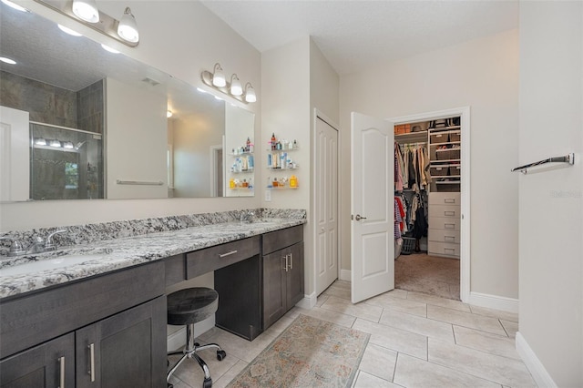 bathroom featuring a stall shower, baseboards, tile patterned floors, a walk in closet, and vanity