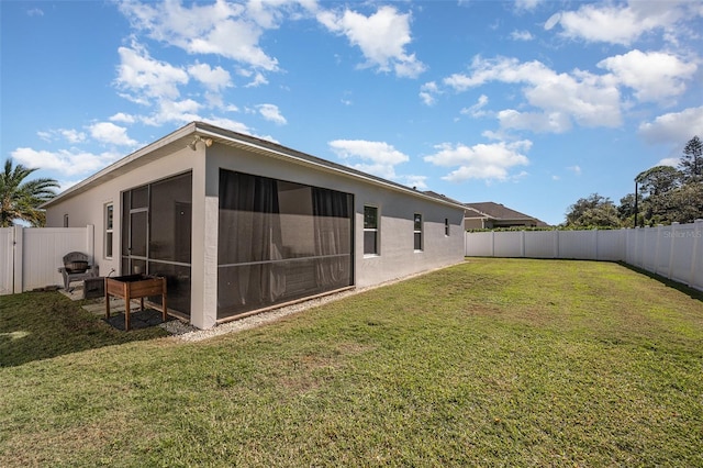 rear view of property with a sunroom, a fenced backyard, a yard, and stucco siding