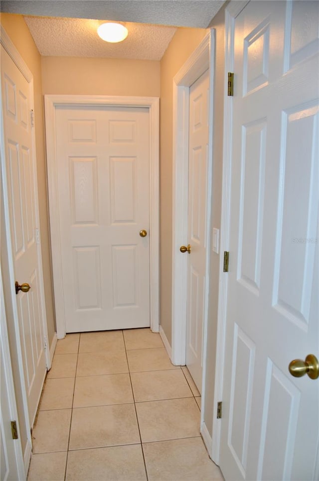 corridor featuring light tile patterned floors, a textured ceiling, and baseboards