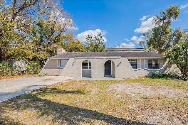 ranch-style home with a chimney, a front lawn, and stucco siding