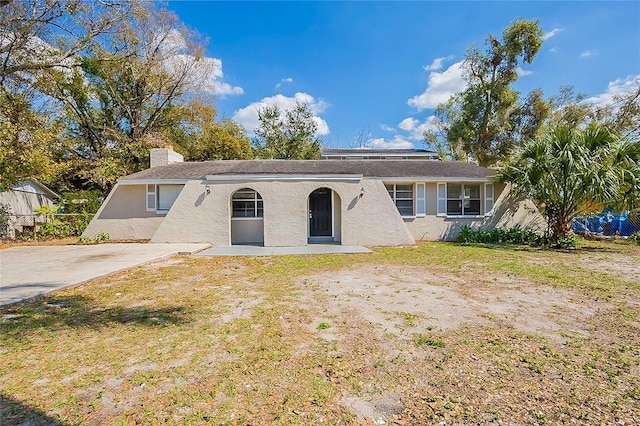 ranch-style home with a front yard, a chimney, and stucco siding