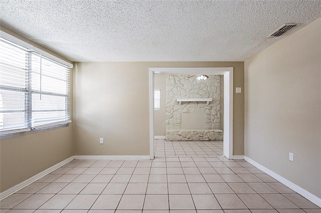 unfurnished room featuring a textured ceiling, a stone fireplace, light tile patterned flooring, and visible vents