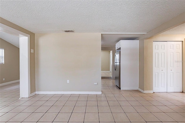 spare room with light tile patterned floors, baseboards, visible vents, and a textured ceiling