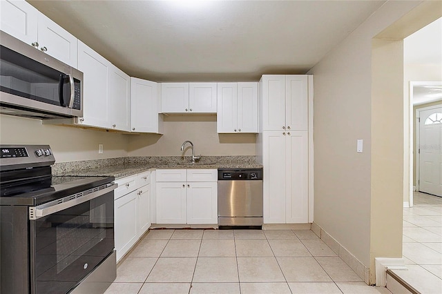 kitchen with light tile patterned floors, appliances with stainless steel finishes, white cabinetry, a sink, and light stone countertops