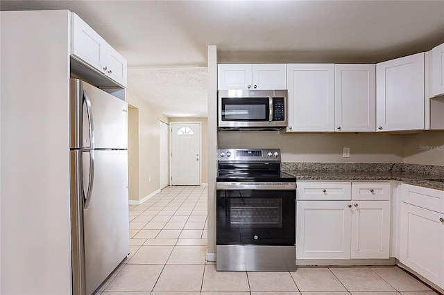 kitchen with light tile patterned floors, appliances with stainless steel finishes, white cabinetry, dark stone counters, and baseboards