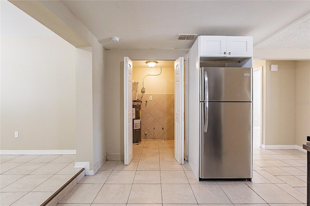 kitchen with water heater, visible vents, freestanding refrigerator, white cabinets, and light tile patterned flooring