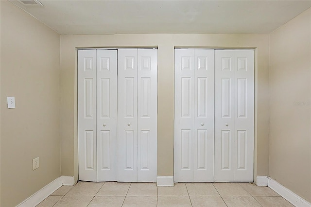 unfurnished bedroom with light tile patterned floors, two closets, and baseboards