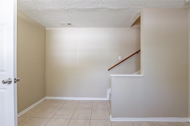 unfurnished room featuring stairs, a textured ceiling, light tile patterned flooring, and visible vents