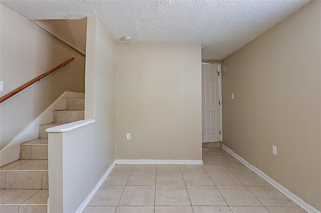 interior space with light tile patterned floors, stairway, a textured ceiling, and baseboards