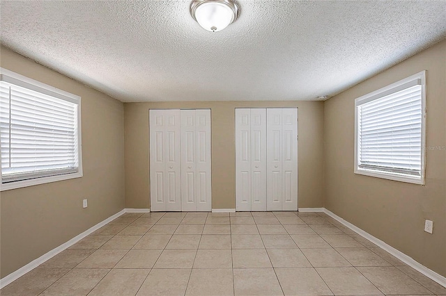 unfurnished bedroom featuring light tile patterned floors, a textured ceiling, baseboards, and multiple closets