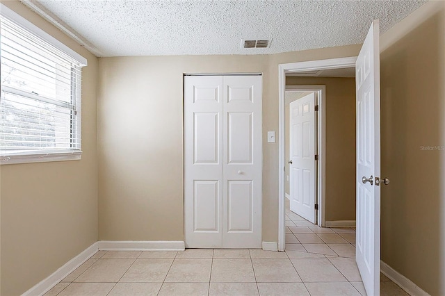 unfurnished bedroom featuring light tile patterned floors, a textured ceiling, visible vents, and a closet