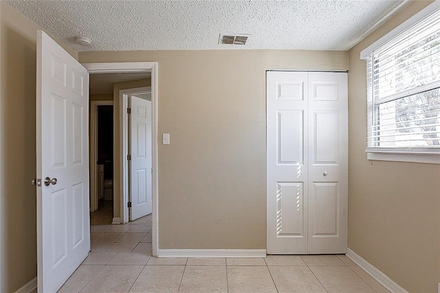 unfurnished bedroom with a closet, visible vents, baseboards, and light tile patterned floors