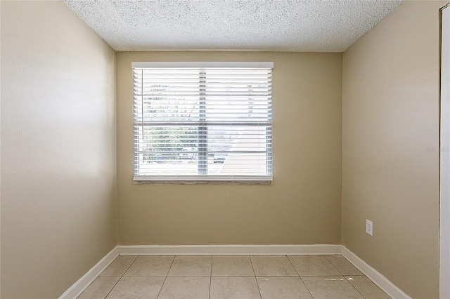 spare room with a textured ceiling, light tile patterned flooring, and baseboards