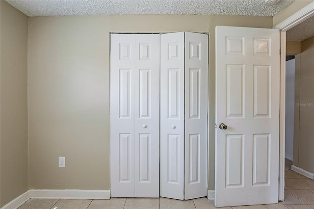 unfurnished bedroom with light tile patterned floors, a textured ceiling, baseboards, and a closet