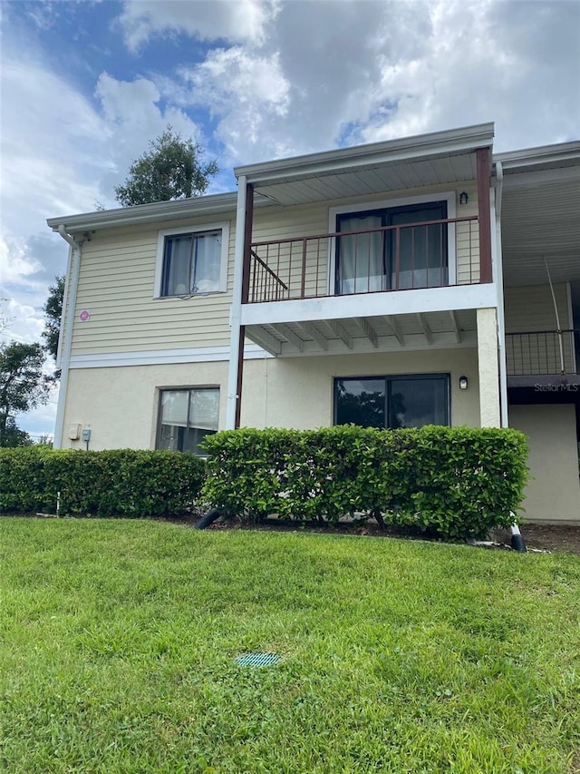 back of property with a balcony, a lawn, and stucco siding