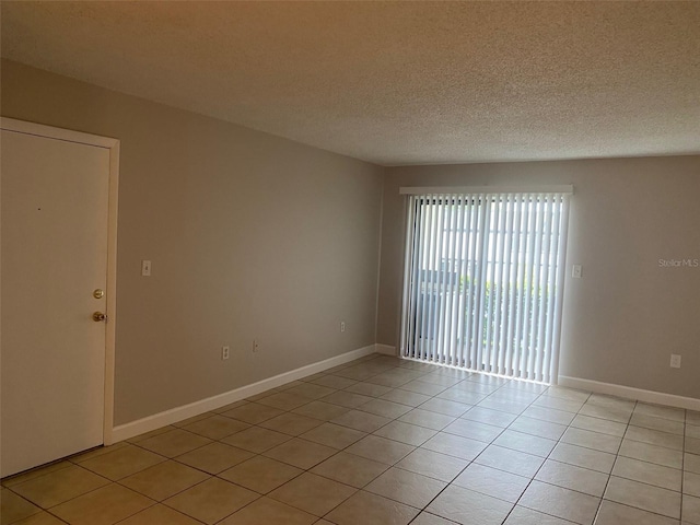 spare room with a textured ceiling, light tile patterned flooring, and baseboards