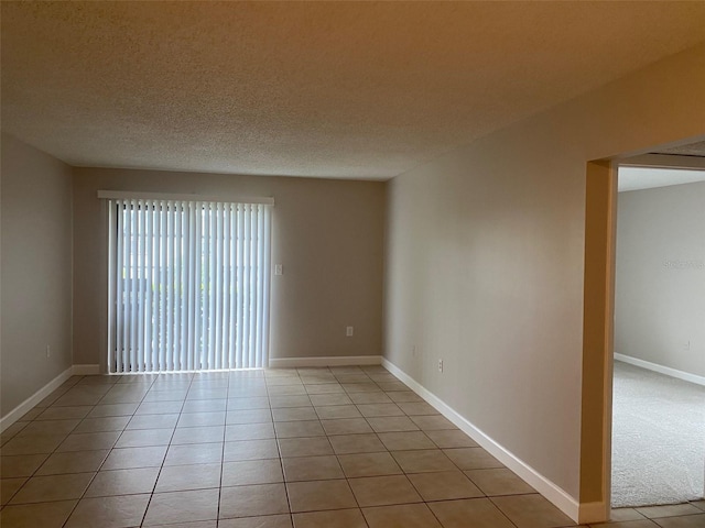 unfurnished room with light tile patterned floors, a textured ceiling, and baseboards