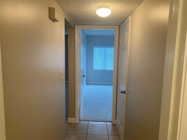 hall featuring light tile patterned flooring, a textured ceiling, and baseboards