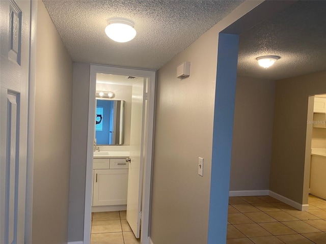 corridor featuring a sink, a textured ceiling, baseboards, and light tile patterned floors