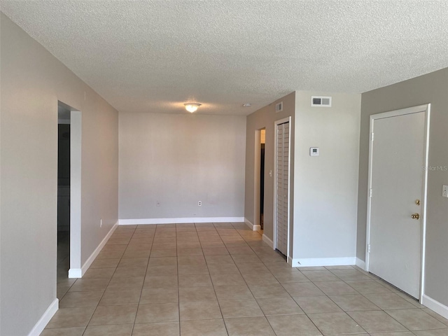 unfurnished room featuring light tile patterned floors, a textured ceiling, visible vents, and baseboards