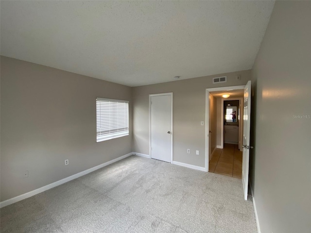 unfurnished bedroom featuring baseboards, a textured ceiling, visible vents, and carpet flooring