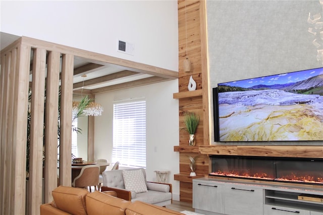 interior space with a towering ceiling, a lit fireplace, visible vents, and beam ceiling