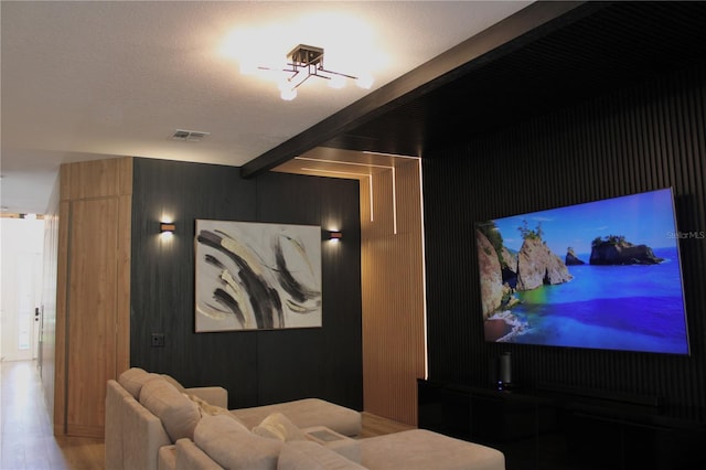 home theater room with a textured ceiling, beam ceiling, visible vents, and light wood-style floors