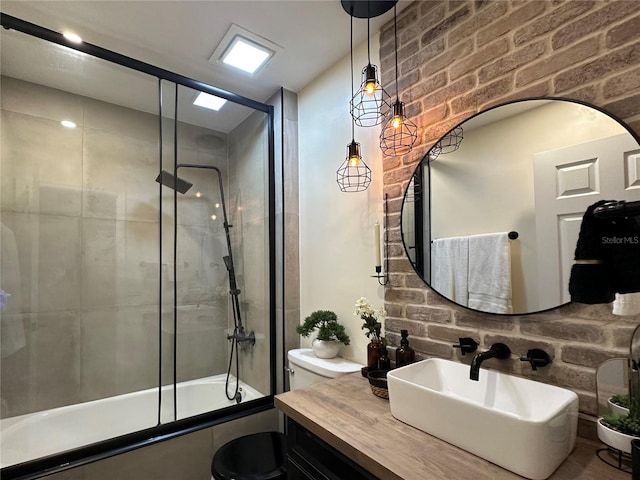 full bath featuring toilet, brick wall, bath / shower combo with glass door, and vanity