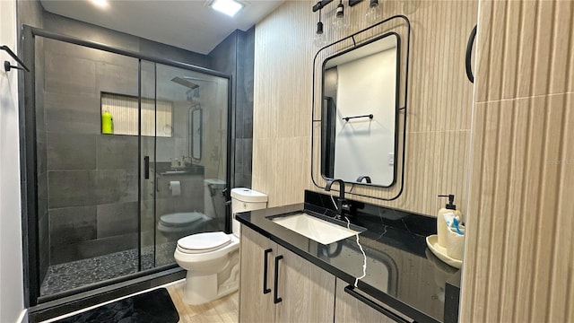 bathroom with toilet, a stall shower, tile walls, and vanity