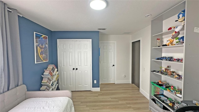 bedroom featuring a textured ceiling, visible vents, baseboards, a closet, and light wood-type flooring