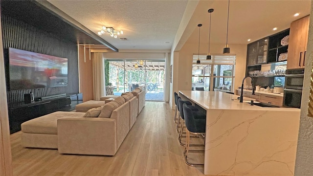 kitchen featuring light stone counters, pendant lighting, open floor plan, a sink, and light wood-type flooring