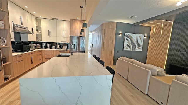 kitchen with open shelves, modern cabinets, light stone countertops, fridge with ice dispenser, and pendant lighting