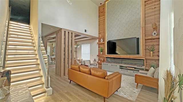 living area featuring light wood-style floors, visible vents, a high ceiling, and stairs