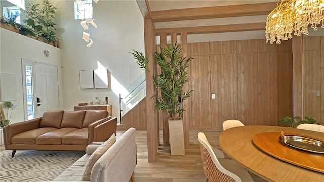 interior space with light wood-style flooring, wooden walls, a high ceiling, beamed ceiling, and an inviting chandelier