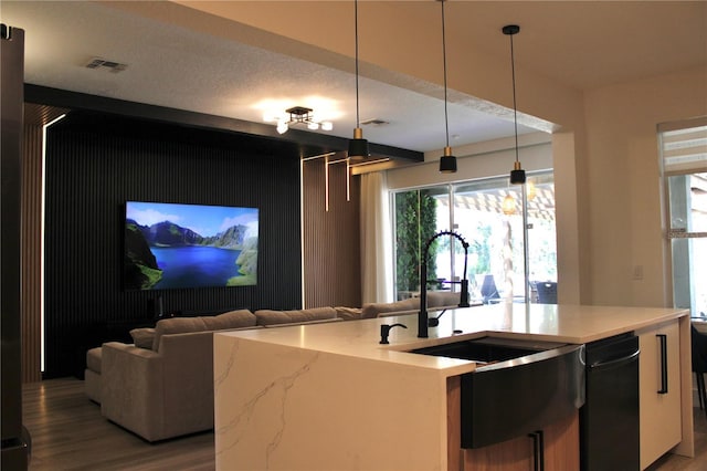 kitchen with light stone counters, decorative light fixtures, a sink, visible vents, and a center island with sink