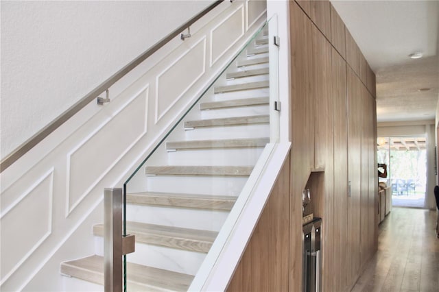 stairs with wainscoting, a decorative wall, and wood finished floors