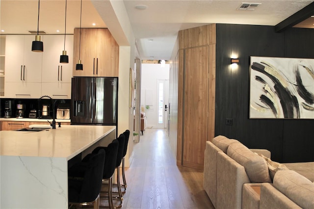 kitchen featuring visible vents, black fridge with ice dispenser, white cabinets, modern cabinets, and a kitchen breakfast bar