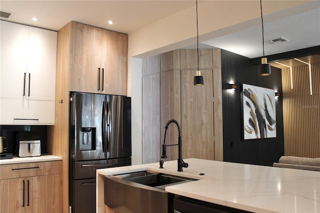 kitchen with light stone counters, pendant lighting, white cabinets, modern cabinets, and stainless steel fridge with ice dispenser