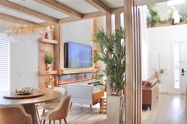 interior space with light wood finished floors, a chandelier, beam ceiling, and a glass covered fireplace