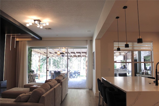 living area with a textured ceiling, a wealth of natural light, visible vents, and light wood-style floors