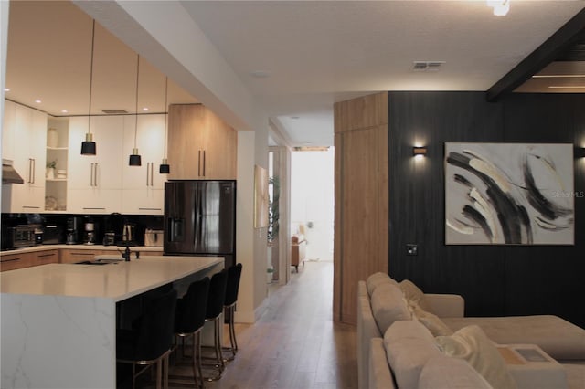 kitchen with wood finished floors, visible vents, a kitchen breakfast bar, modern cabinets, and decorative light fixtures