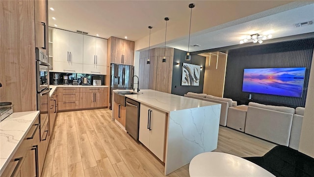 kitchen with an island with sink, open floor plan, decorative light fixtures, stainless steel appliances, and white cabinetry