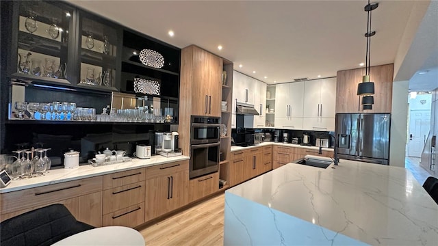 kitchen with pendant lighting, modern cabinets, black refrigerator with ice dispenser, a sink, and light stone countertops