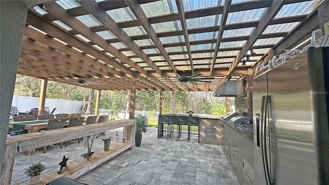 view of patio / terrace with area for grilling, an outdoor kitchen, ceiling fan, fence, and outdoor wet bar