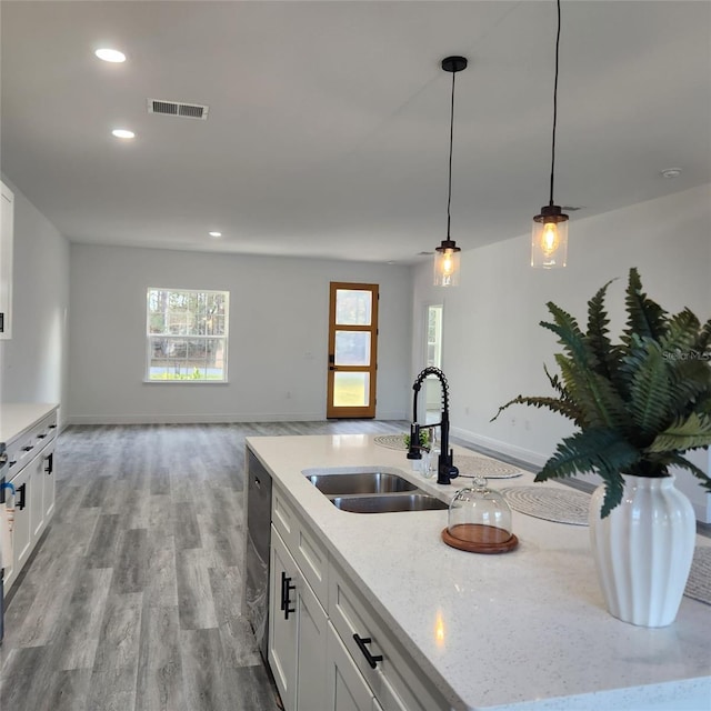 kitchen with visible vents, light stone counters, hanging light fixtures, white cabinetry, and a sink