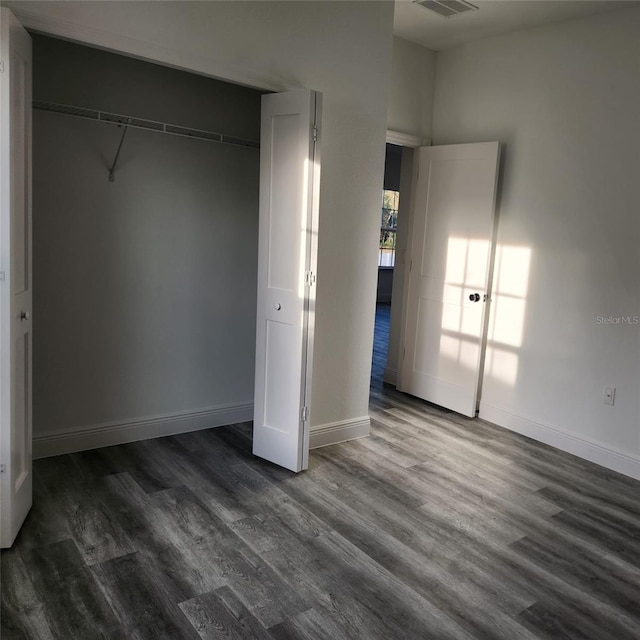 unfurnished bedroom featuring dark wood-style floors, baseboards, visible vents, and a closet