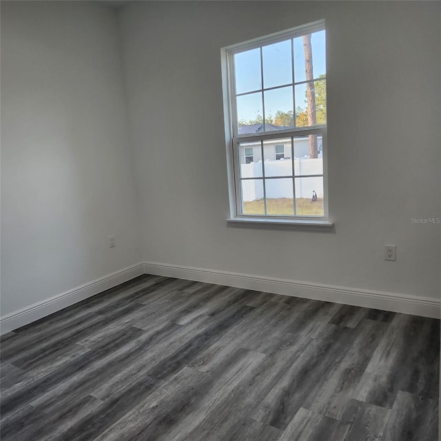 empty room with dark wood-style floors, a wealth of natural light, and baseboards