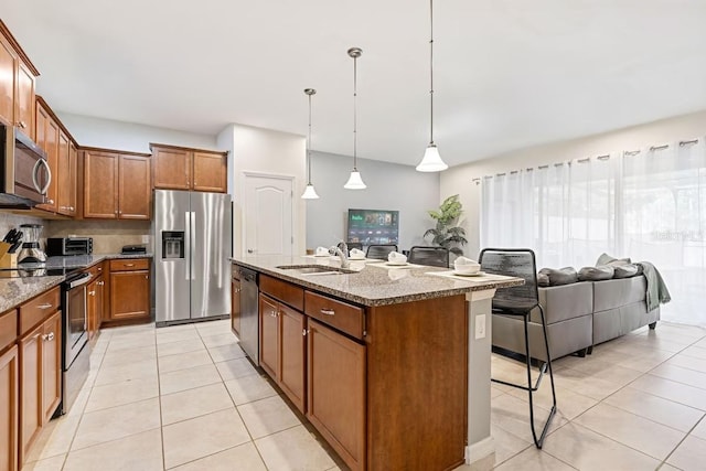 kitchen featuring light stone counters, a sink, appliances with stainless steel finishes, a center island with sink, and pendant lighting